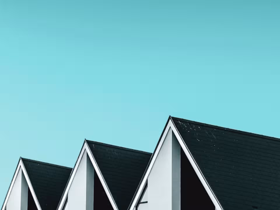 Três casas geminadas com telhados pretos em duas águas e céu azul-esverdeado ao fundo.