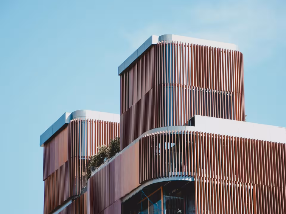A parte superior de uma casa moderna com brises de madeira na fachada e céu azul ao fundo.